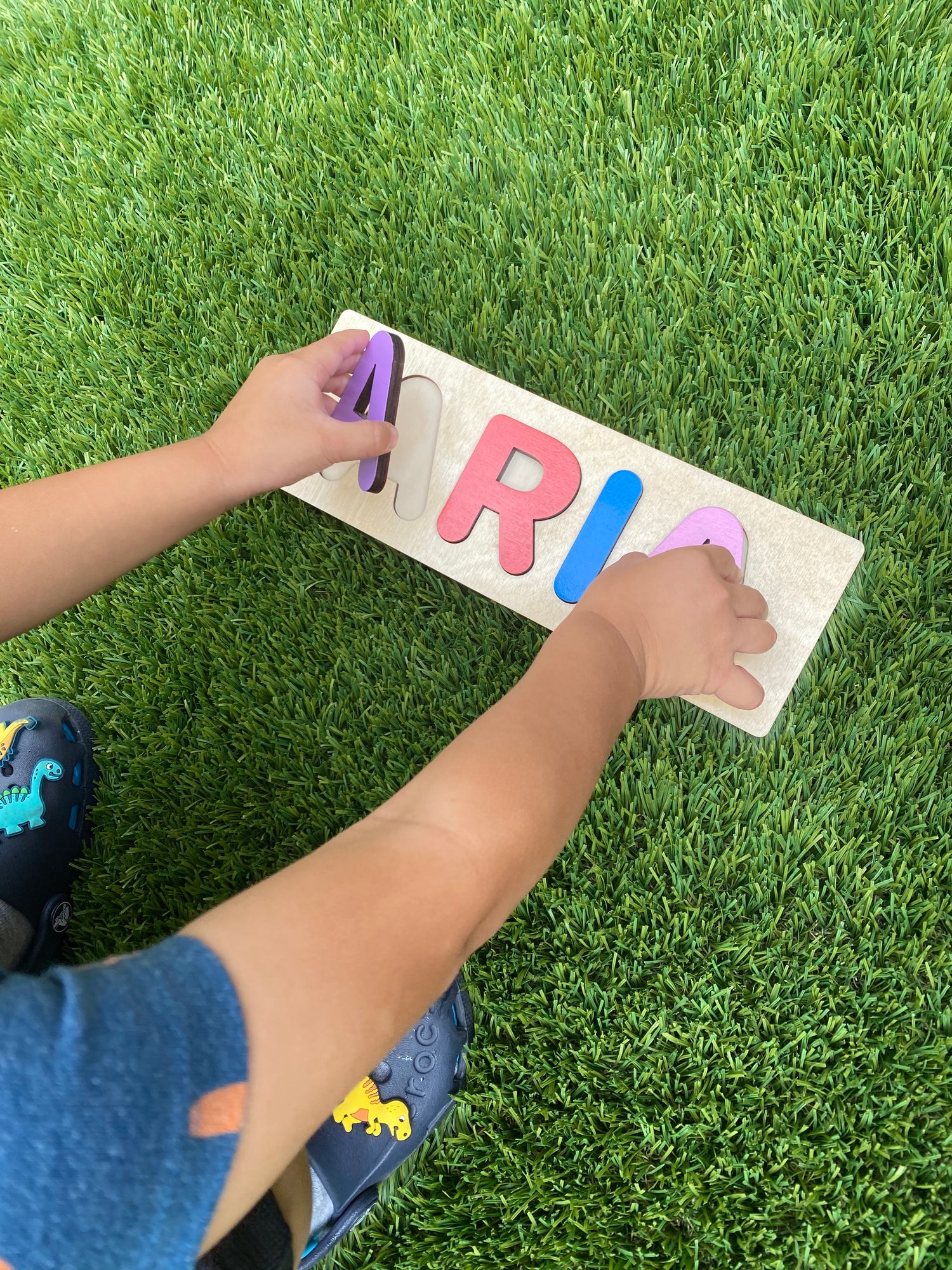Kid playing with name block and puzzle colored in rainbow floral colors on grass