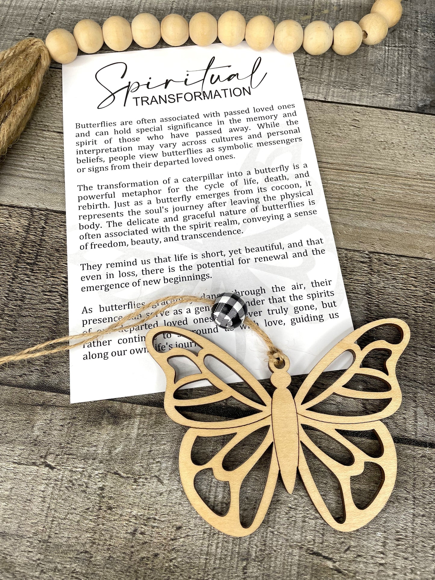 A gold-colored butterfly-shaped charm with a story card that says 'Spiritual Transformation' and other inspirational quotes, placed on a wooden surface.