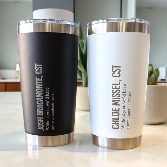 Two insulated tumblers, one black and one white, with engraved text on a kitchen counter.