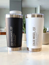 Two insulated tumblers, one black and one white, with engraved text on a kitchen counter.