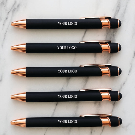Five black and rose gold pens with 'YOUR LOGO' text on a marble surface