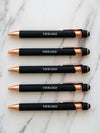 Five black and rose gold pens with 'YOUR LOGO' text on a marble surface