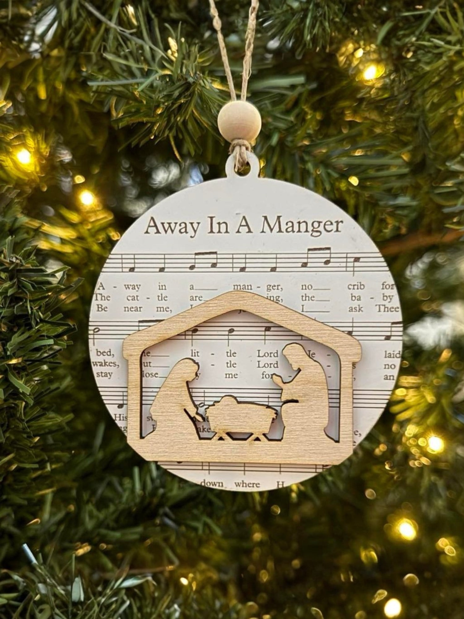 Decorative Christmas ornament with nativity scene and 'Away in a Manger' text on a tree.
