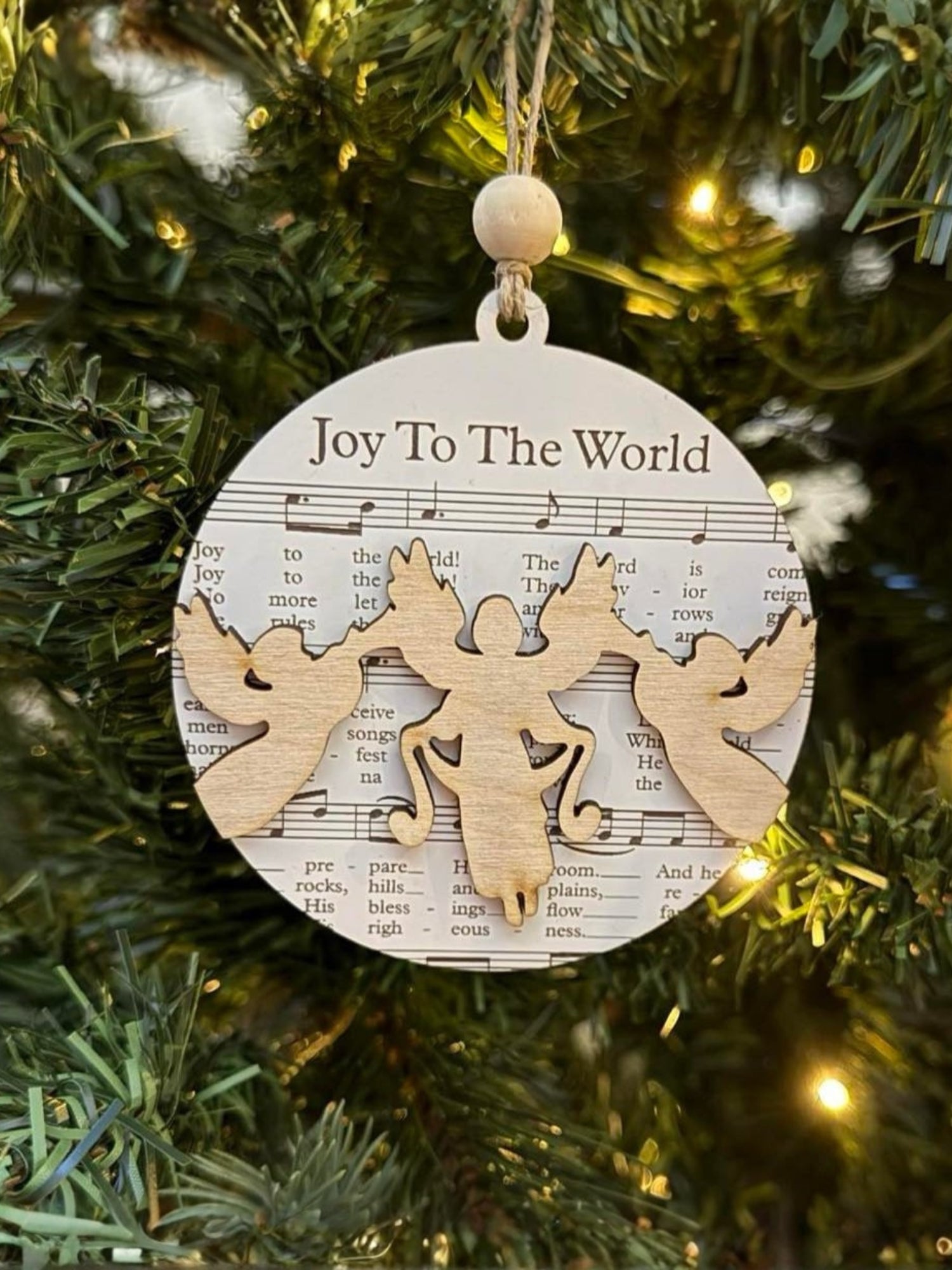 Decorative Christmas ornament with 'Joy To The World' text and angel design on a tree.