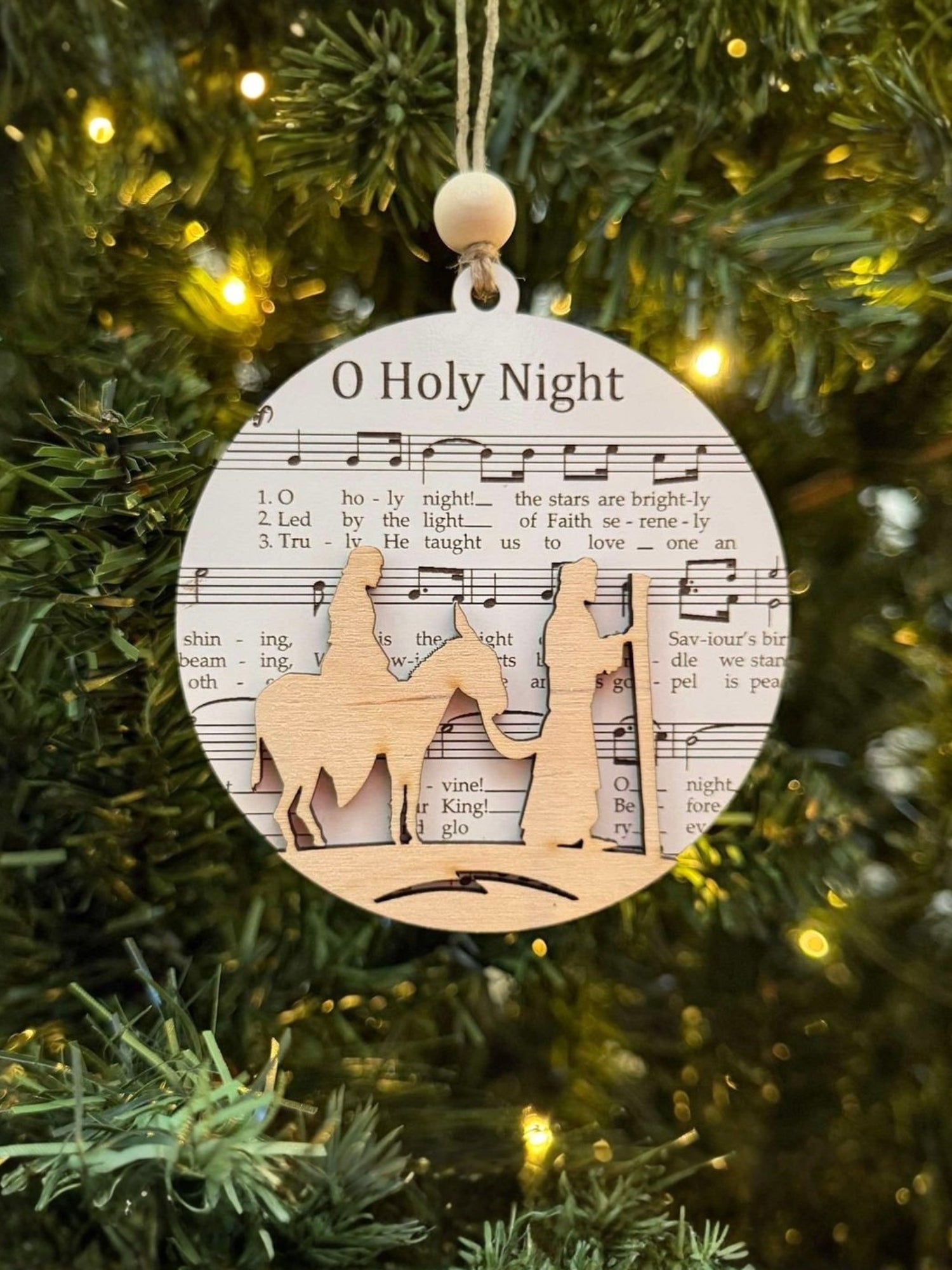 Decorative Christmas ornament with nativity scene and 'O Holy Night' text on a tree.