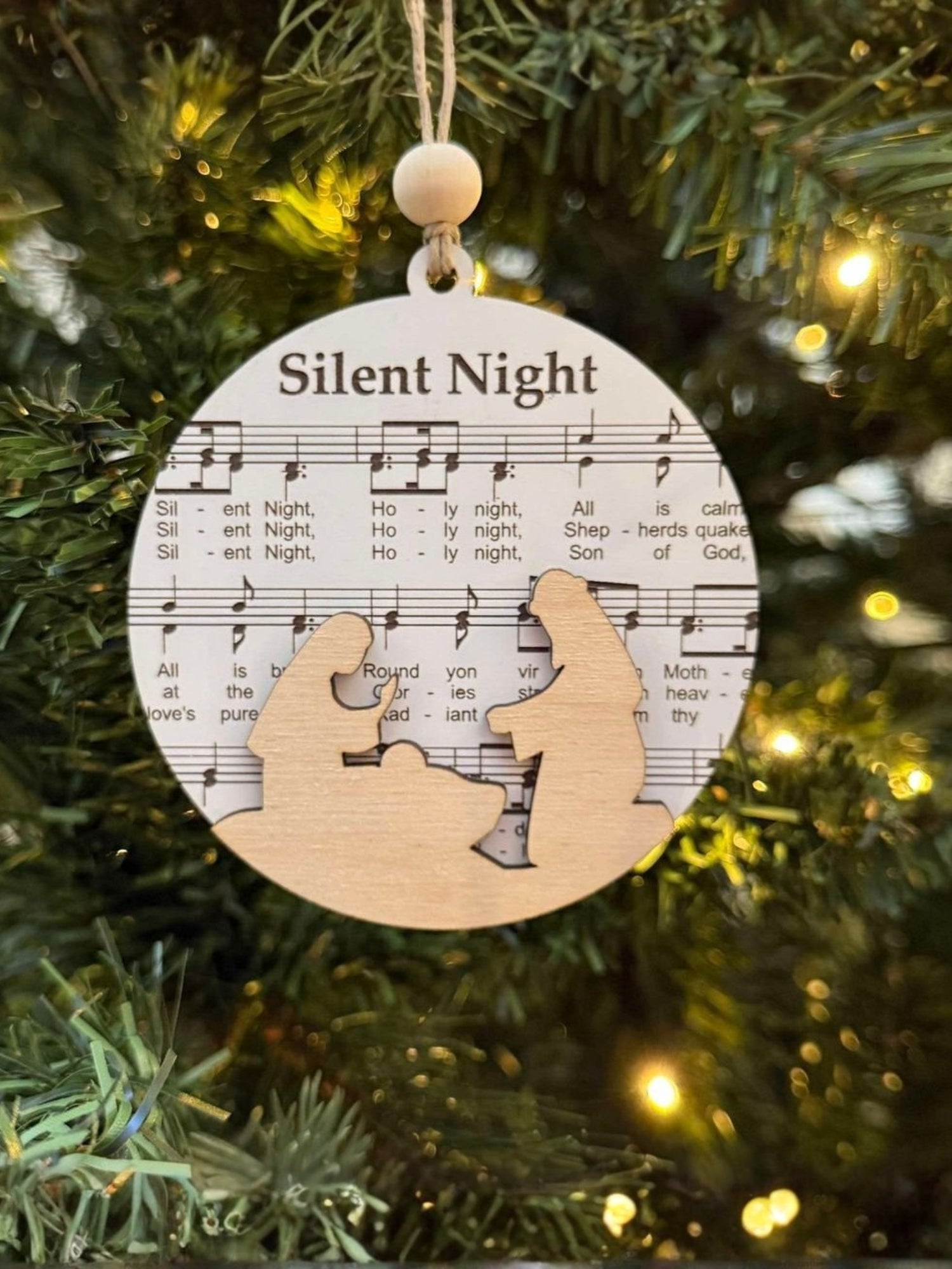 Decorative ornament with 'Silent Night' lyrics on a Christmas tree.