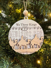 Wooden ornament with 'We Three Kings' text and nativity scene on a Christmas tree.