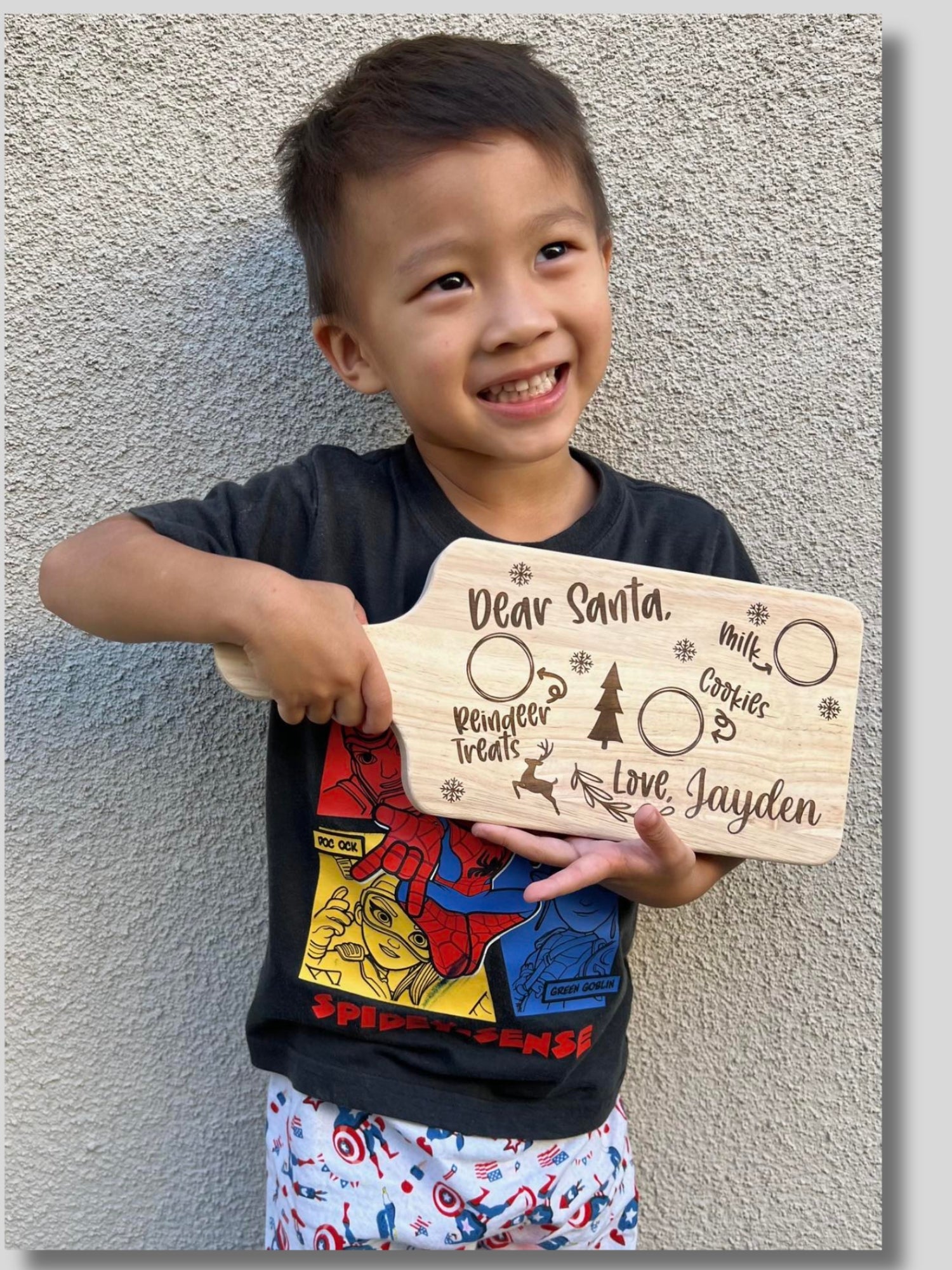 Child holding a personalized Christmas list sign against a textured wall.