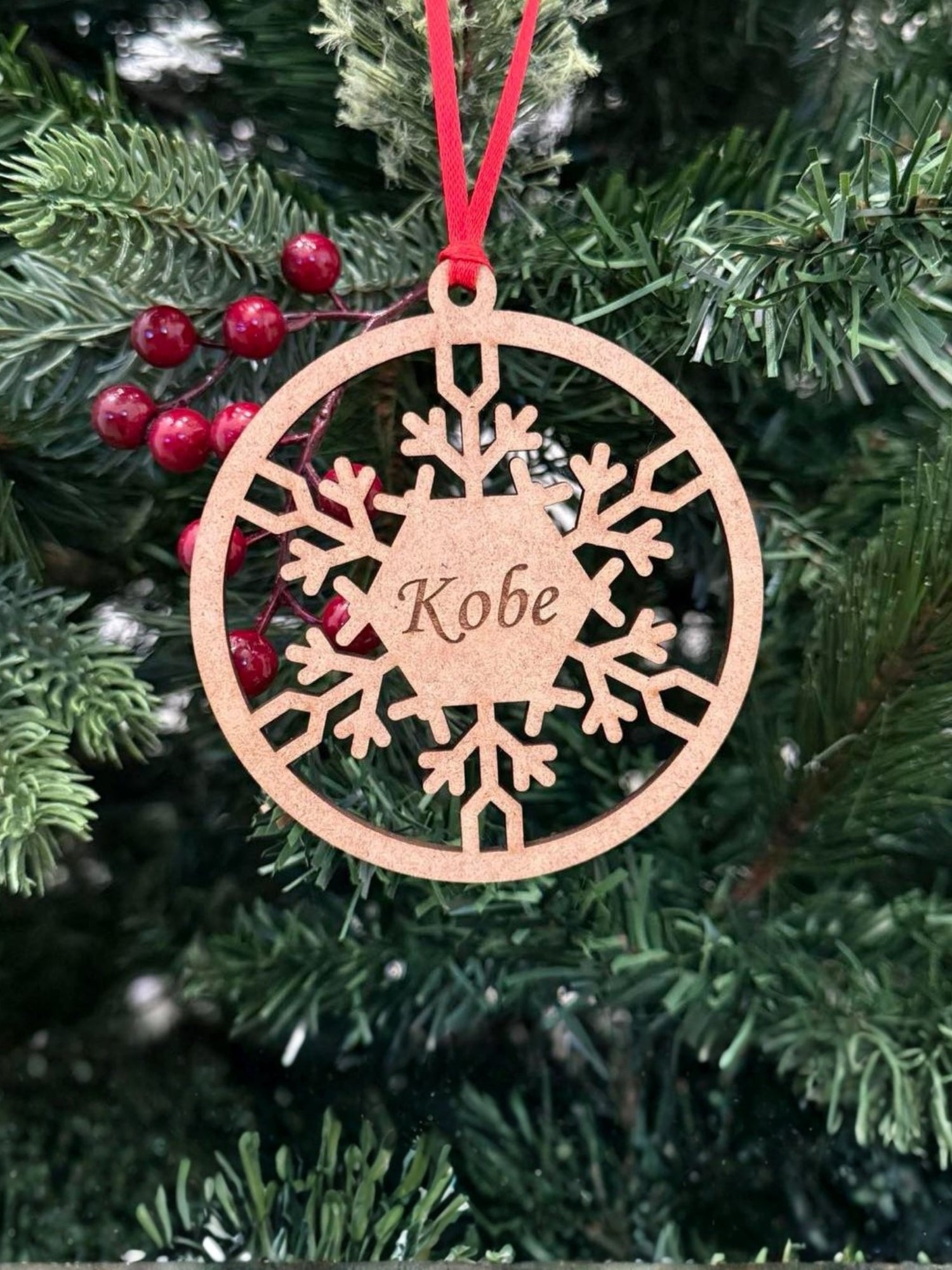 Wooden snowflake ornament with 'Kobe' engraved, hanging on a Christmas tree.