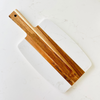 A personalized cheese board made of wood and marble, with a white marble surface and a wooden handle, resting on a marble surface.