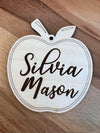 Wooden apple-shaped tag with 'Silvia Mason' engraved on a wooden surface