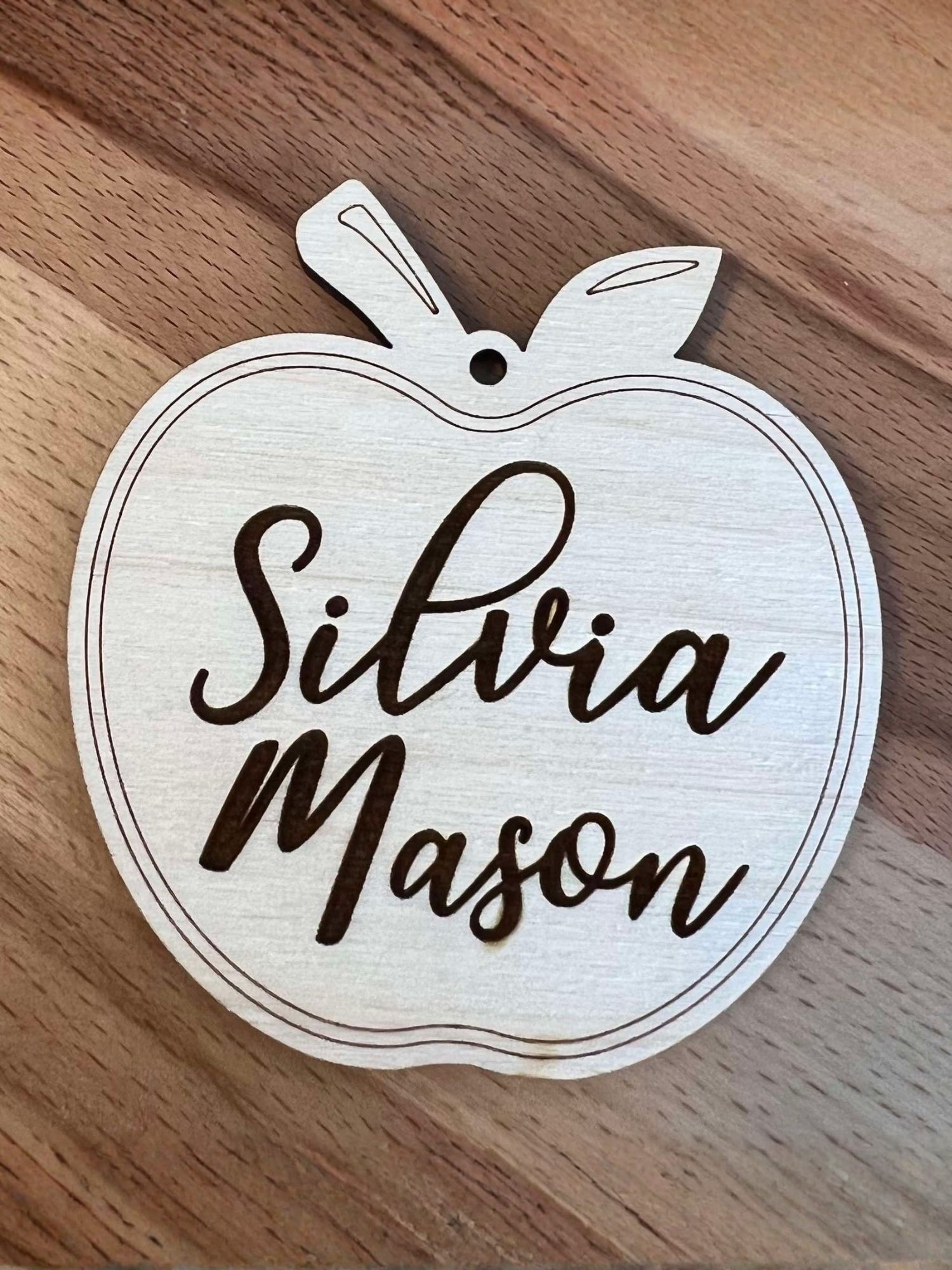 Wooden apple-shaped tag with 'Silvia Mason' engraved on a wooden surface