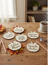 Personalized name tags shaped like apples on a wooden table with a cup of tea and pencils.